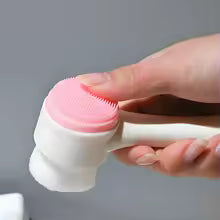 Hand holding a pink silicone facial cleansing brush with soft bristles for deep pore cleaning and skincare routine
